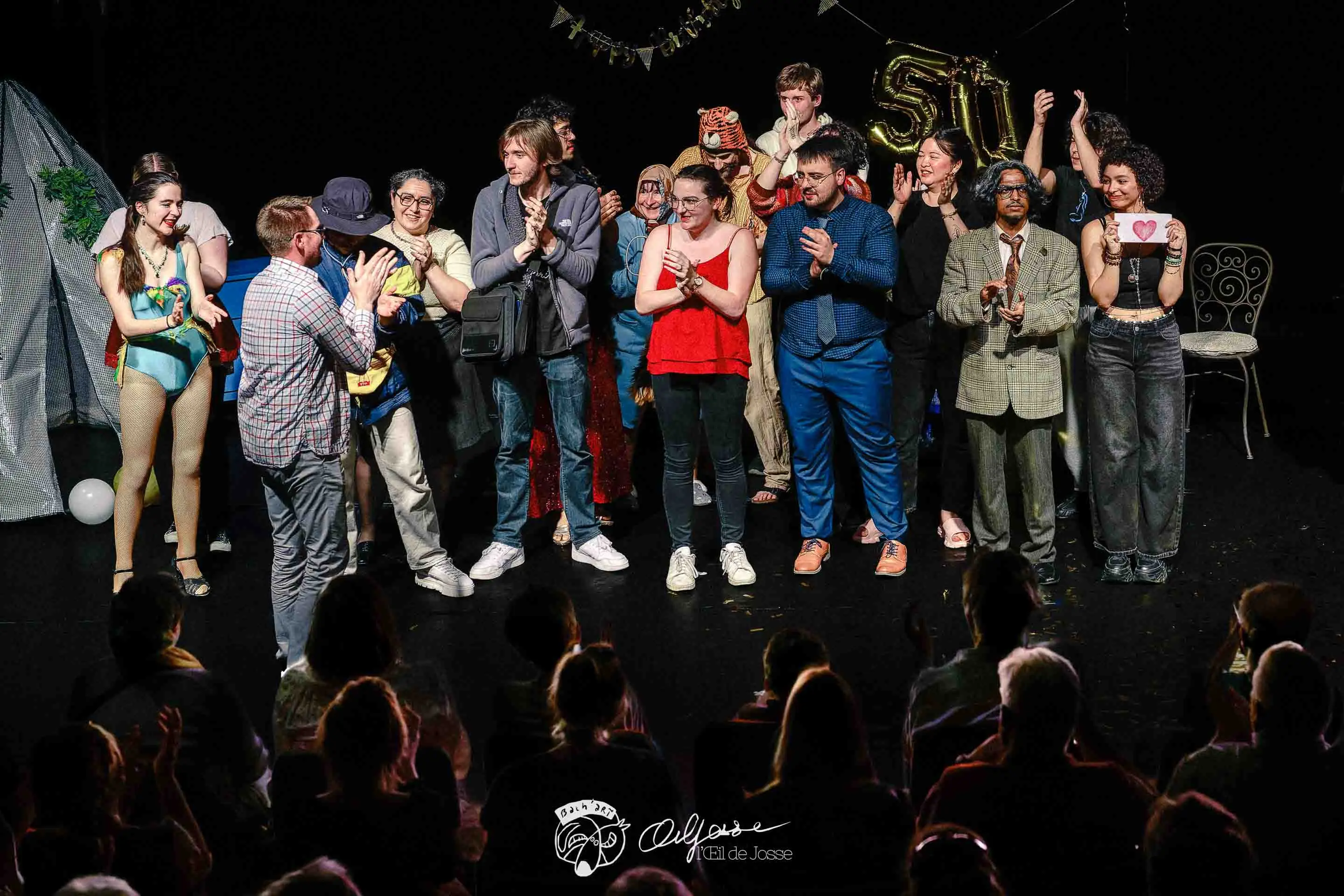 La troupe au grand complet salue le public sous les applaudissements, des ballons dorés en fond de scène.