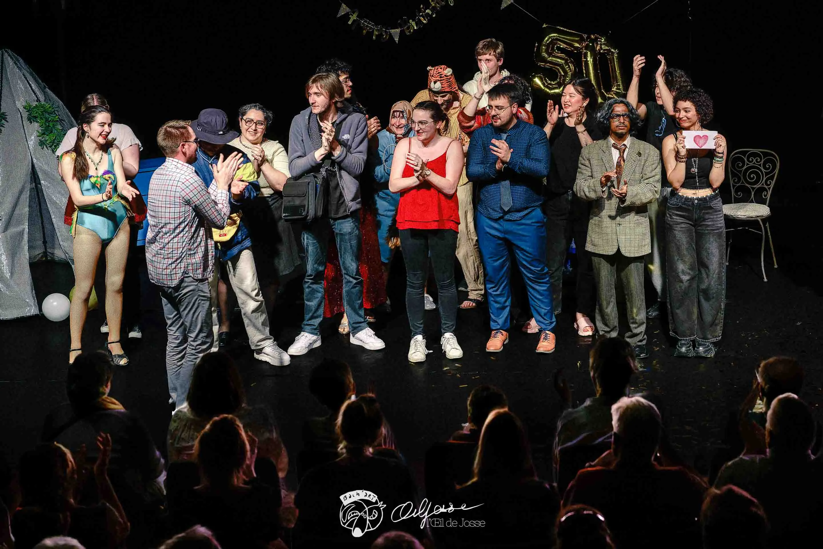 La troupe au grand complet salue le public sous les applaudissements, des ballons dorés en fond de scène.