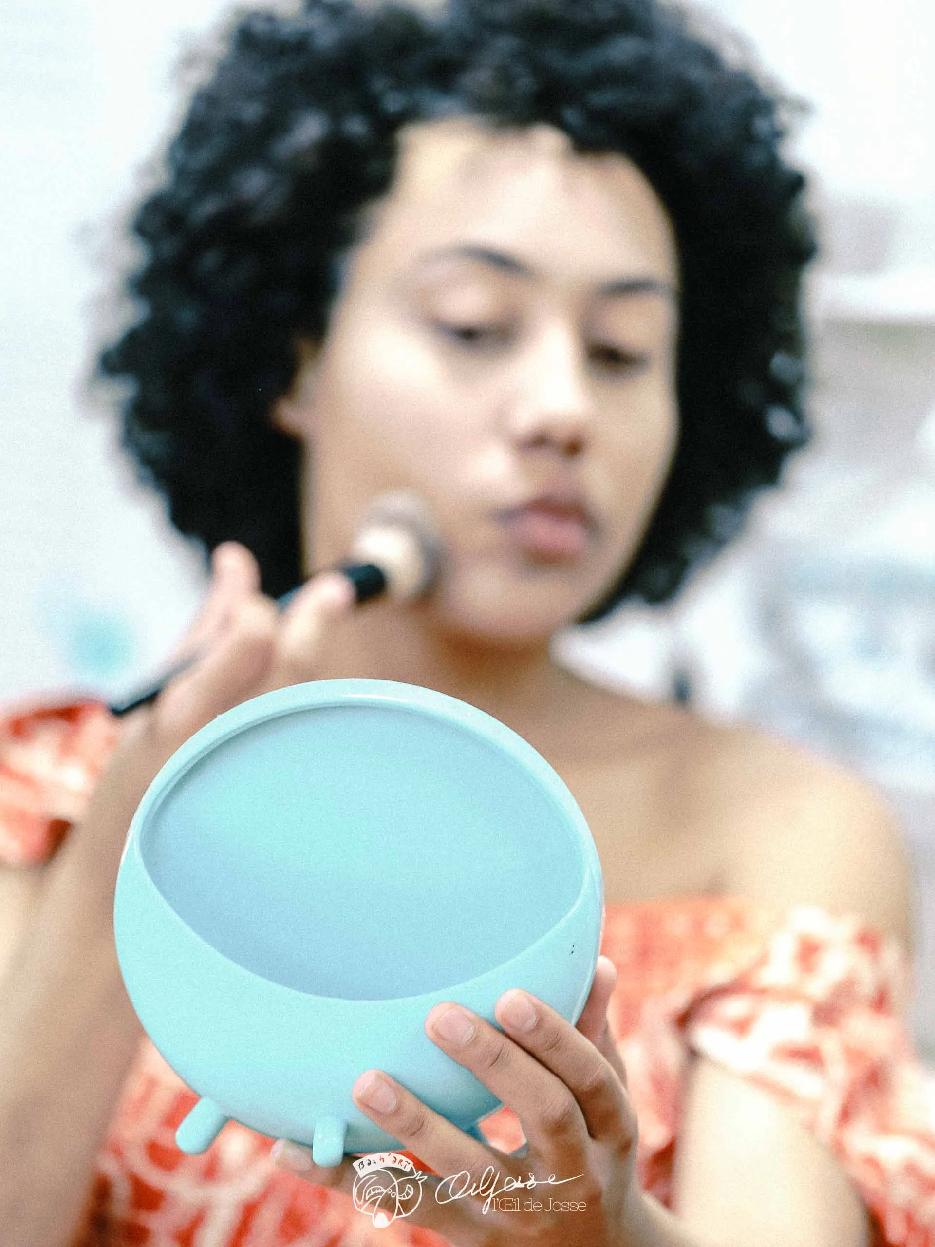 Une comédienne se poudre le visage face à un miroir turquoise.